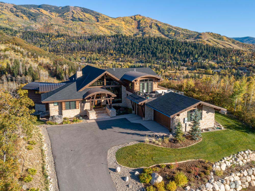 Drone photo of stone home with wood accents and beautiful mountain views.