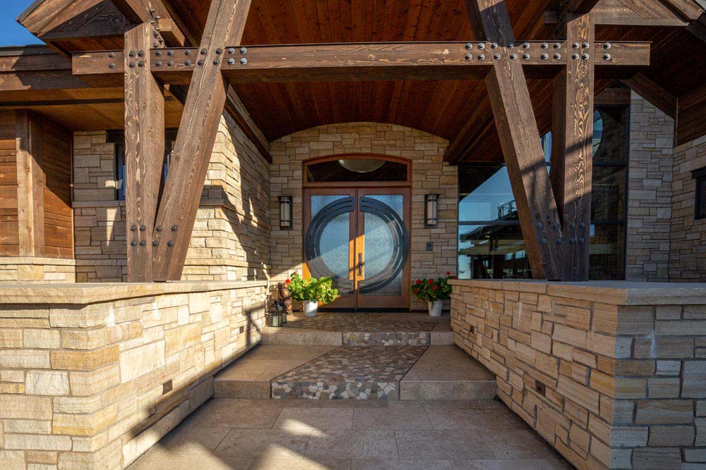 Outside entry into custom mountain home with large beams and double door entry.
