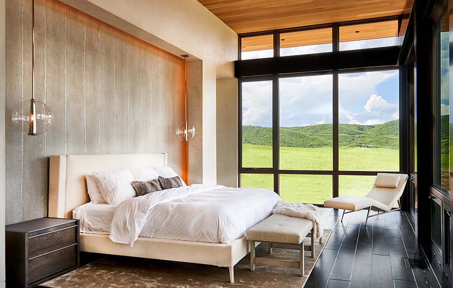 Modern bedroom with large windows looking out onto a green field.