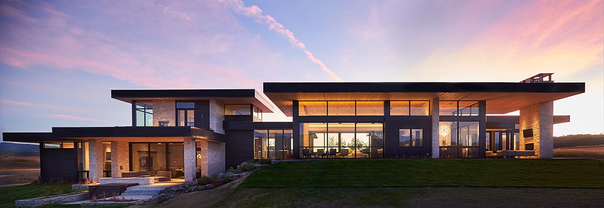 Modern home lit up with sunset in the background.