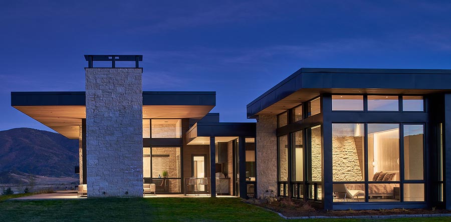 Modern home with a lot of windows at night lit up inside.
